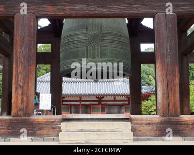 De dessous de la vieille grande cloche près de l'ancien temple coloré Avec des colonnes parmi les plantes vertes au Japon Banque D'Images