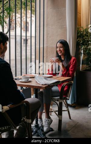 Calme décontracté jeune couple assis à la table près de la fenêtre et boire du café et parler tout en prenant le petit déjeuner au café Banque D'Images