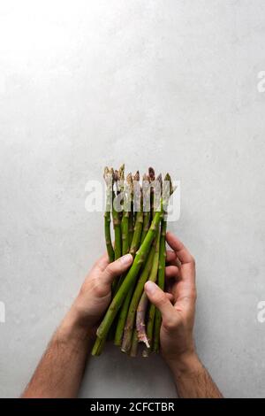 Vue de dessus de crop anonyme chef tenue de groupe de frais asperges vertes tout en préparant les aliments à la table en marbre gris cuisine Banque D'Images