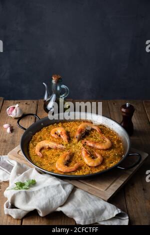 Grand angle de la grande poêle en métal de tout en appétissant paella avec crevettes rôties sur une table rustique dans la composition avec vintage bouteille d'huile et serviette dans la cuisine à la maison Banque D'Images