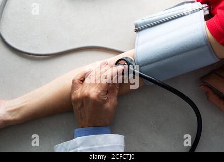 Depuis le dessus du médecin de récolte avec le stéthoscope assis à la table dans la salle médicale et mesurer la pression artérielle avec le tonomètre pendant travailler à l'hôpital pendant l'éclosion du coronavirus Banque D'Images