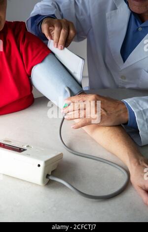 Depuis le dessus du médecin de récolte avec le stéthoscope assis à la table dans la salle médicale et mesurer la pression artérielle avec le tonomètre pendant travailler à l'hôpital pendant l'éclosion du coronavirus Banque D'Images