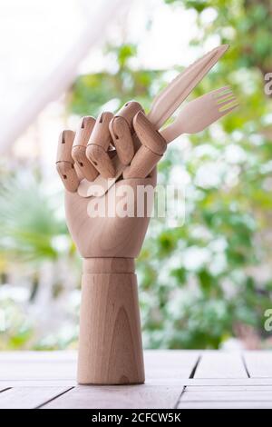Main de mannequin créative avec fourchette jetable et couteau garni branche de persil vert placée sur une table dans le jardin Banque D'Images