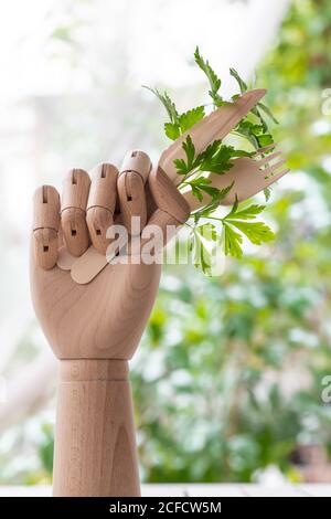 Main de mannequin créative avec fourchette jetable et couteau garni branche de persil vert placée sur une table dans le jardin Banque D'Images