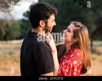 homme embrassant une femme enceinte souriante sur fond de parc vert pittoresque par beau temps Banque D'Images