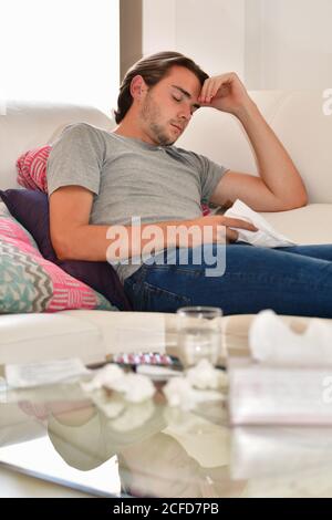 Beau jeune homme prenant une sieste et tenant une serviette tout en étant allongé sur un canapé. Concept détente et repos. Banque D'Images