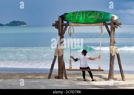 Une femme thaïlandaise de tourisme dans les temps de Covid-19, de détente sur une balançoire sur une plage de Patong autrement vide, Phuket, Thaïlande Banque D'Images