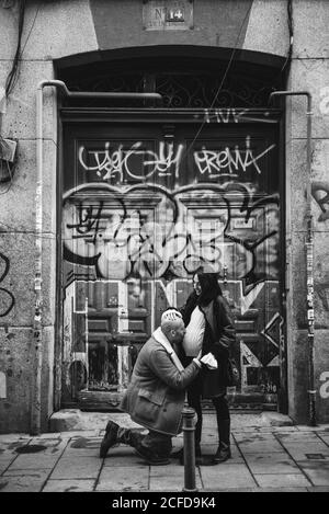 Vue latérale en noir et blanc de l'homme adulte s'agenouillant et embrasser le ventre de la femme enceinte contre le mur de graffiti grundy rue de la ville Banque D'Images