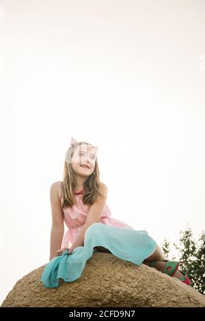 De dessous de la petite fille dans la robe et les oreilles de chat assis sur un rocher haut dans la nature, à l'abri de la vue Banque D'Images