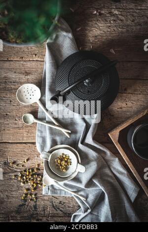 De la composition ci-dessus de la théière noire et bol blanc et herbes de camomille sur une table en bois Banque D'Images