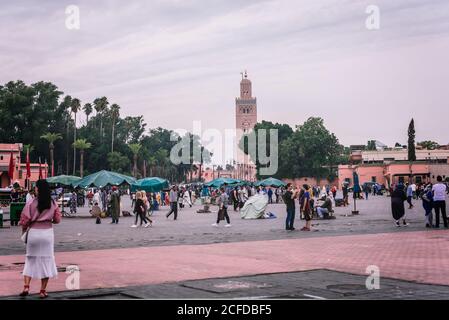 Marrakech, Maroc - 22 octobre 2018 : marchands assis sous des parasols tandis que les touristes marchent à Jemaa el-Fnaa Banque D'Images