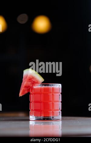 Smoothie au melon d'eau frais et sain dans une tasse en verre décorée d'un morceau de fruits sur la surface réfléchie Banque D'Images