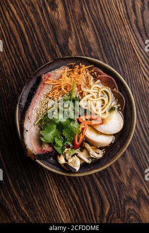 Vue de dessus de délicieux ramen et nouilles et légumes dans un bol sur une table en bois Banque D'Images