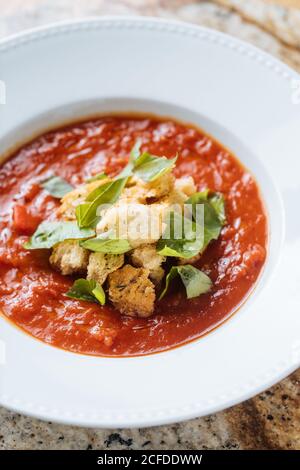 Soupe de tomates fraîches appétissantes rouges avec des légumes verts sur une assiette blanche sur un stand en marbre dans le café Banque D'Images