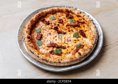 Au-dessus de la pizza juteuse servie avec du fromage, des herbes et des tomates séchées sur la table dans le restaurant Banque D'Images