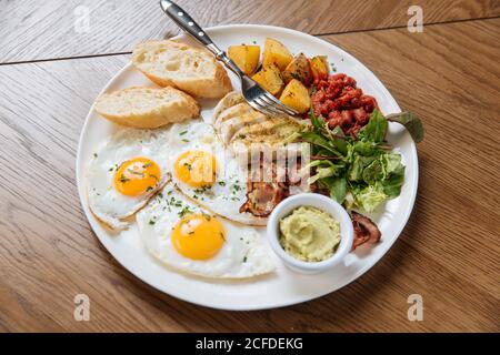 Vue de dessus du petit déjeuner anglais servi avec des œufs frits et bacon avec toasts et légumes sur une table en bois Banque D'Images