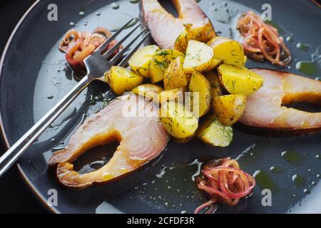 Des morceaux de poisson mariné et d'oignons rôtis pommes de terre disposées sur une plaque près de la fourchette Banque D'Images