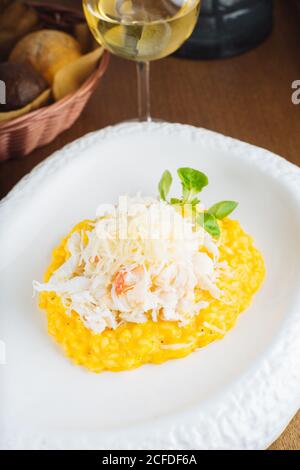 Du dessus du risotto traditionnel au safran avec du parmesan garni avec des herbes vertes servies sur une assiette blanche sur une table en bois avec un verre de vin blanc Banque D'Images