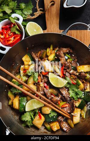 Vue de dessus de l'appétissant oriental épicé sauté viande avec courgettes et poivrons rouges garnis de citron vert frais et de coriandre Banque D'Images