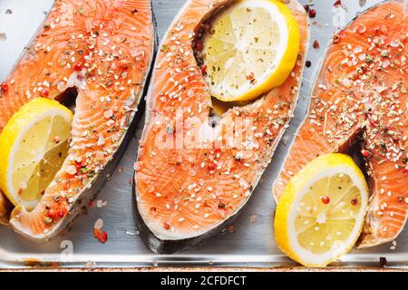 Vue de dessus de steaks de saumon frais avec assaisonnement aromatique et tranches de citron placées sur une plaque de cuisson métallique Banque D'Images