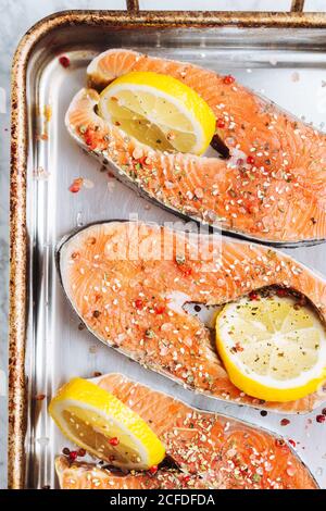 Vue de dessus de steaks de saumon frais avec assaisonnement aromatique et tranches de citron placées sur une plaque de cuisson métallique Banque D'Images