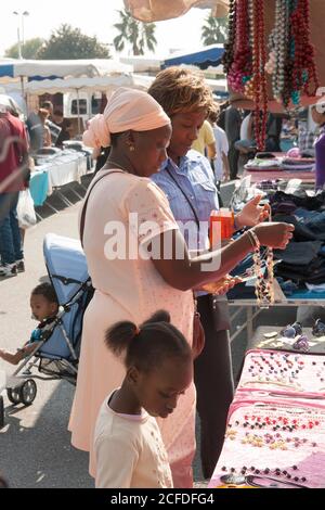 La famille noire, la femme, la mère, la fille et les petits-enfants font leurs courses sur le marché local du week-end. Ils font leur choix parmi des perles et des colliers. Banque D'Images