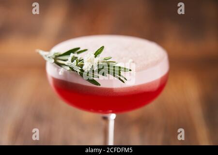 De dessus de verre élégant avec alcool rouge cocktail consiste de blancs d'œufs de gin jus de lime et sirop de framboise décorés au romarin Banque D'Images