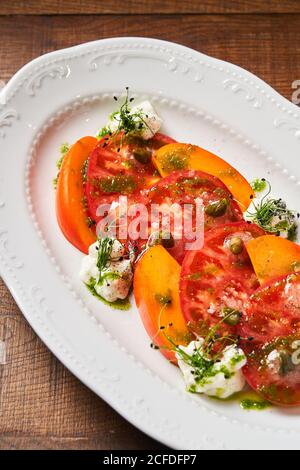 De dessus de tranches de tomates rouges fraîches et de mangue sur une assiette blanche décorée de fromage féta aux herbes et de pesto sauce Banque D'Images