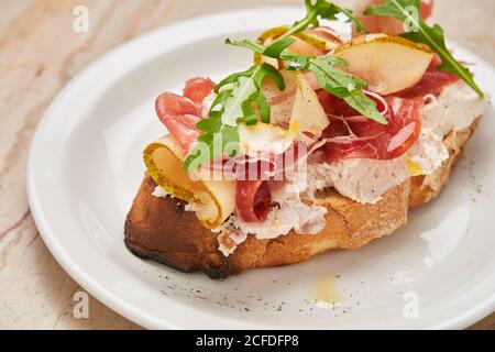 Du dessus du jambon avec des tranches de poire rôties pain avec fromage à la crème décoré d'arugula sur une assiette blanche Banque D'Images