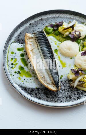 De la partie supérieure du poisson rôti avec une sauce à la crème délicieuse et des herbes fraîches placées sur l'assiette sur fond blanc Banque D'Images