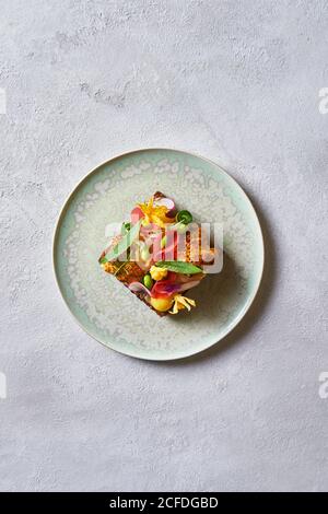Du dessus vue du dessus délicieux sandwich décoré avec des tranches de légumes et les fleurs et placées sur l'assiette sur la table blanche dans café Banque D'Images