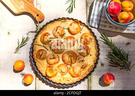 Tarte à la crème aigre d'abricot sur une table de jardin avec décoration au romarin d'abricot, bol d'abricot et planche à découper coupée au bord de l'image. Banque D'Images