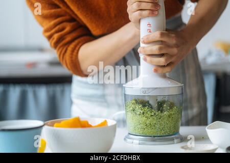 Faire cuire à la récolte en préparant les aliments et en mélangeant les légumes verts en blanc mixeur sur table dans la cuisine légère Banque D'Images