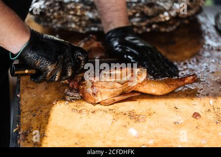Du dessus du chef de récolte en gants avec coupe au couteau poulet frit sur une table en bois dans la stalle du marché Banque D'Images
