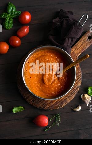 Sauce tomate maison dans une casserole et ingrédients sur une table rustique en bois, vue sur le dessus, espace copie. Faire de la sauce tomate italienne biologique ou de la soupe. Banque D'Images