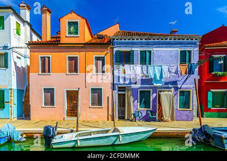 Île de Burano maisons colorées avec murs multicolores et vêtements suspendus, remblai de canal étroit d'eau avec bateaux de pêche, province de Venise, région de Vénétie, Italie du Nord. Carte postale Burano Banque D'Images