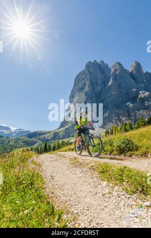 Cycliste avec vélo électrique (e-bike) pédalant au pied de Sassolungo Langkofel, Val Gardena, Grödental, Tyrol du Sud, Dolomites, Italie Banque D'Images