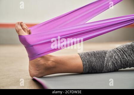 Vue latérale de la femelle pieds nus dans les leggings de sport qui étirent les muscles avec bracelet de résistance pendant l'entraînement en salle de sport Banque D'Images