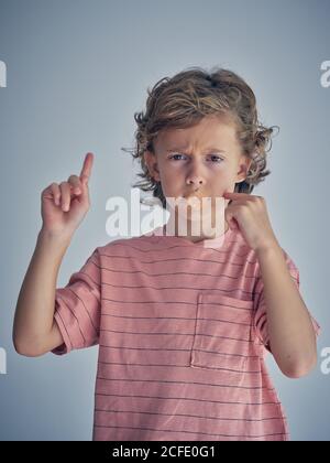 Enfant curieusement réfléchis garder le silence avec du plâtre sur la bouche pendant en pointant le doigt en l'air, demandez à parler et à regarder à l'appareil photo Banque D'Images