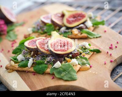 Délicieux sandwichs ouverts colorés faits maison avec des tranches de figues et morceaux de fromage sur du pain de seigle croustillant parmi le vert aromatique feuilles de roquette et fleurs roses Banque D'Images