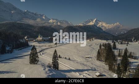 Château d'Elmau en hiver avec des stadels en bois, vue le long des montagnes de Wetterstein vers Alpspitze, Zugspitze et Waxensteine, arbres, ciel bleu, Banque D'Images