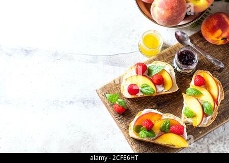 En-cas d'été - sandwichs au fromage à la crème et pêches fraîches sur fond de béton léger. Petit déjeuner d'été maison. Banque D'Images