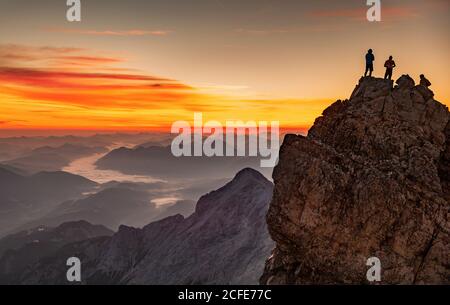 Trois jeunes hommes au sommet du Zugspitze, la plus haute montagne d'Allemagne, au lever du soleil en automne, avec vue sur l'Alpspitze en direction de la vallée de l'Isar, Banque D'Images