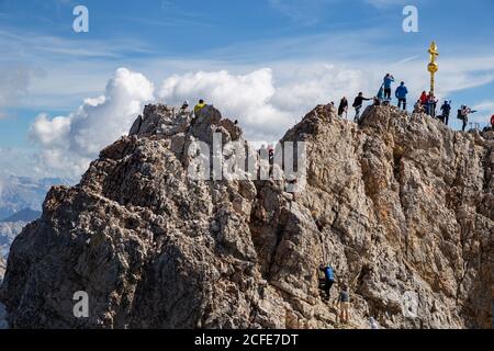 Groupe de personnes sur le sommet de Zugspitz en face de la croix de sommet, ciel bleu, nuages, Zugspitze, Grainau, Garmisch-Partenkirchen, haute-Bavière, Bavière, Banque D'Images