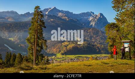 Homme et femme se trouvent devant le panneau d'information touristique, vue sur Garmisch-Partenkirchen et la Große Olympiaschanze jusqu'aux montagnes de Wetterstein Banque D'Images