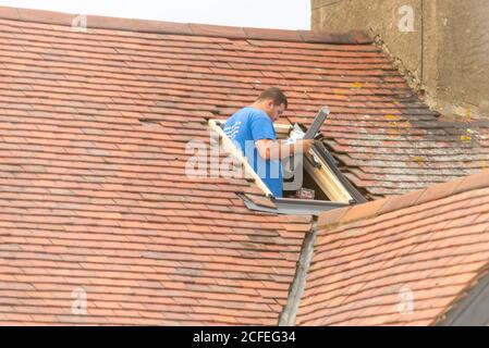 Un constructeur installant une fenêtre de puits de lumière dans le toit d'une propriété à Westcliff sur la mer, Essex, Royaume-Uni, tout en lisant les instructions. Homme de métier blanc Banque D'Images