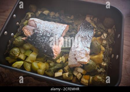 De dessus plat à rôtir avec de grandes pièces de saumon avec peau sur la garniture de légumes et légumes cuits assortis Banque D'Images