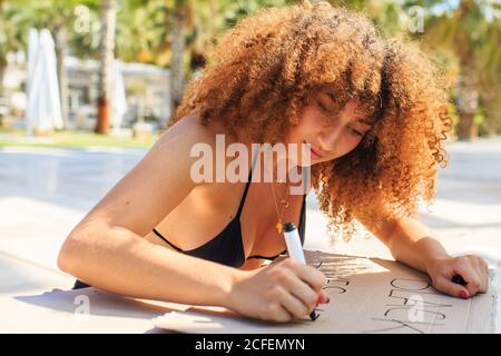 Femme ethnique sérieuse avec la coiffure afro créant carton poster avec inscription black lives matter assise pendant la démonstration Banque D'Images