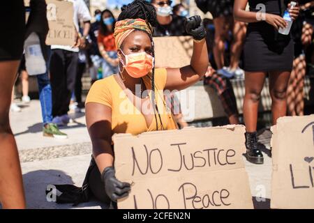 Femme ethnique sérieuse avec la coiffure afro s'agenouillant sur la chaussée avec affiche en carton avec des vies noires matière et aucune justice non inscription à la paix pendant la manifestation dans une ville surpeuplée et le clapping Banque D'Images