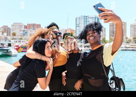 Groupe de filles charismatiques multiraciales debout sur le front de mer et de prendre selfie sur smartphone pendant la promenade en été Banque D'Images